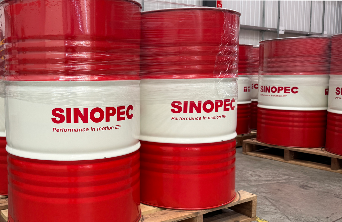 Red and white Sinopec branded metal oil drums stacked on wooden pallets inside a warehouse.